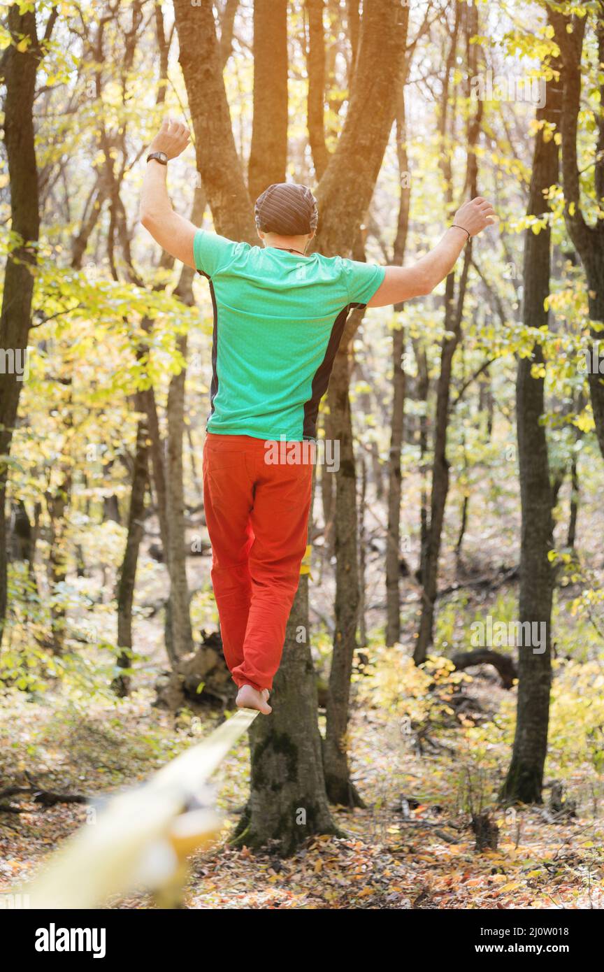 Ein bärtiger Mann im Alter geht an einem sonnigen Nachmittag entlang einer Slackline im Herbstwald. Das Konzept der Freizeit und Erholung von A Stockfoto