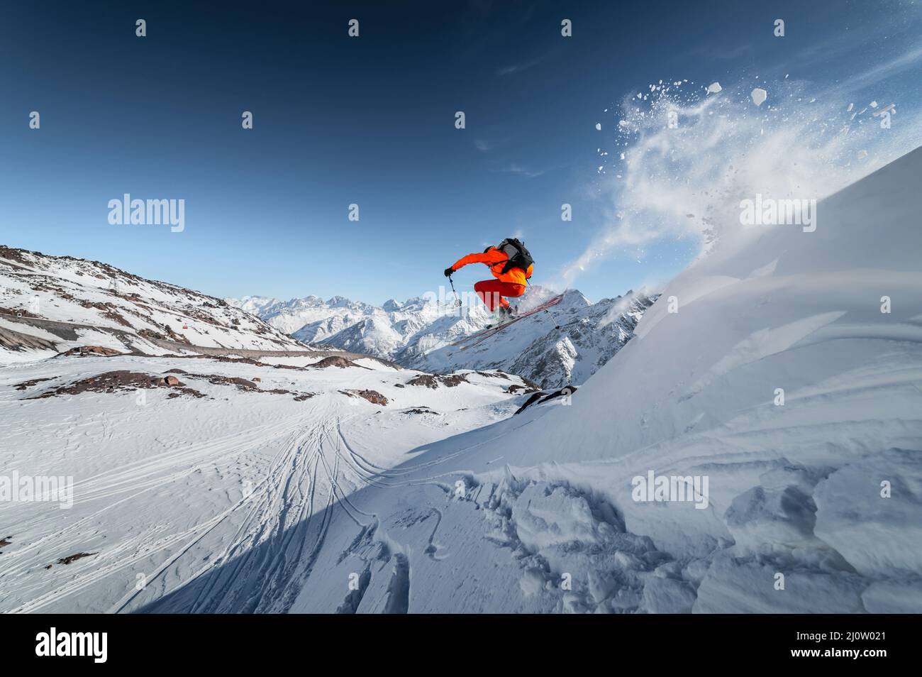 Der Athlet männlich Skifahrer springt von einem schneebedeckten Hang vor der Kulisse einer Berglandschaft mit schneebedeckten Bergen auf einer s Stockfoto