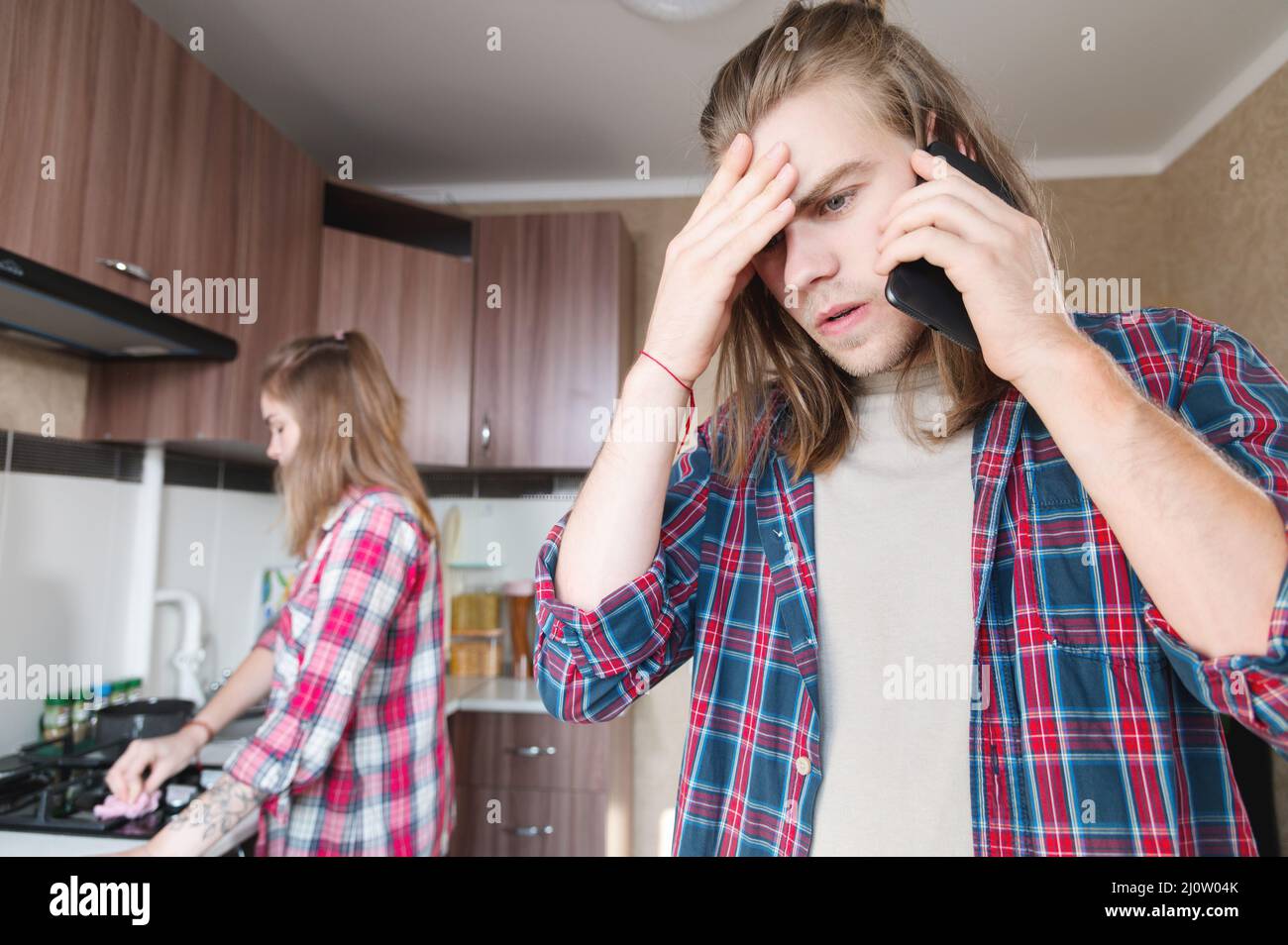 Schwere Störung der langhaarige junge Mann, der in der Küche steht, nutzt sein Mobiltelefon oder bestellt einen Dienst aus dem Internet-Tal Stockfoto