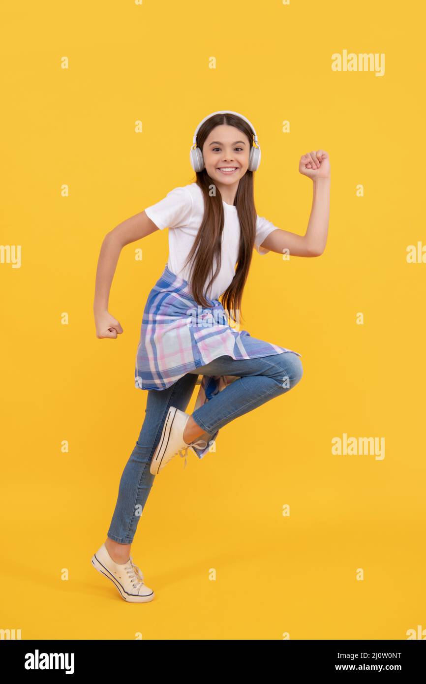 Energisches Teenager-Mädchen läuft, während Musik in Kopfhörern gelben Hintergrund hören, Spaß Stockfoto