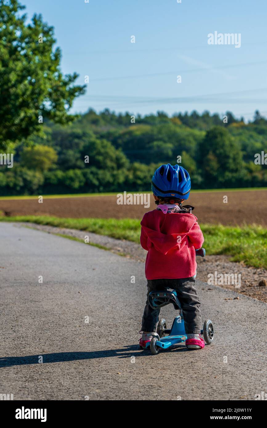 Ein kleines Kind mit einem blauen Fahrradhelm auf einem Roller Stockfoto