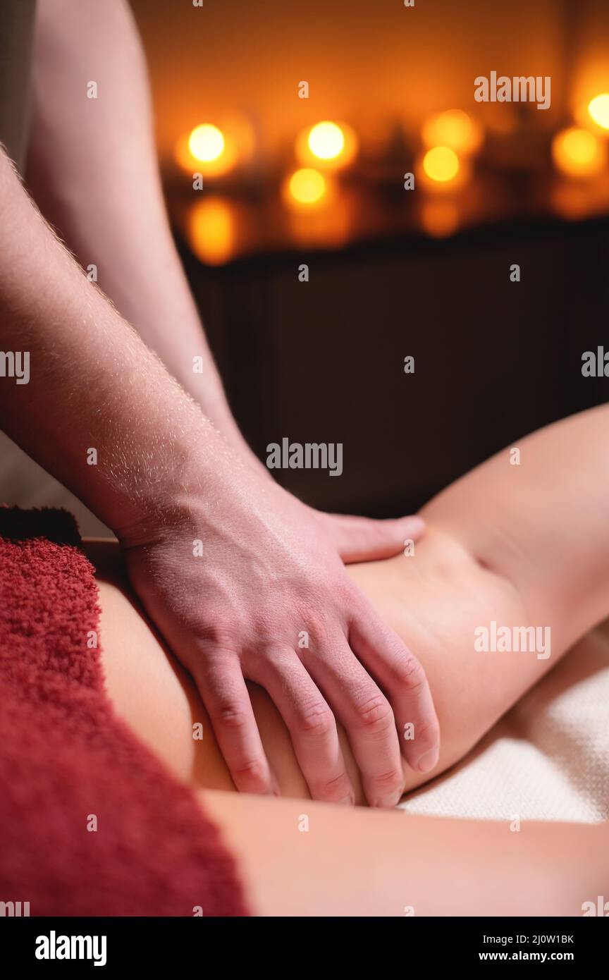 Professionelle Nahaufnahme-Massage der weiblichen Hüfte im dunklen Raum des Spa-Salons vor dem Hintergrund brennender Kerzen. Der Stockfoto