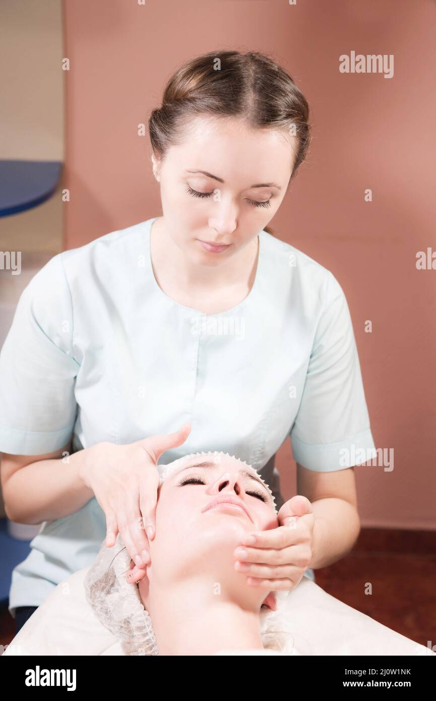 Eine professionelle weibliche Masseurin führt eine Gesichtsmassage für einen Klienten in einem Wellness-Gesichtspflegesalon durch. Das Konzept der Gesichtsmasse Stockfoto