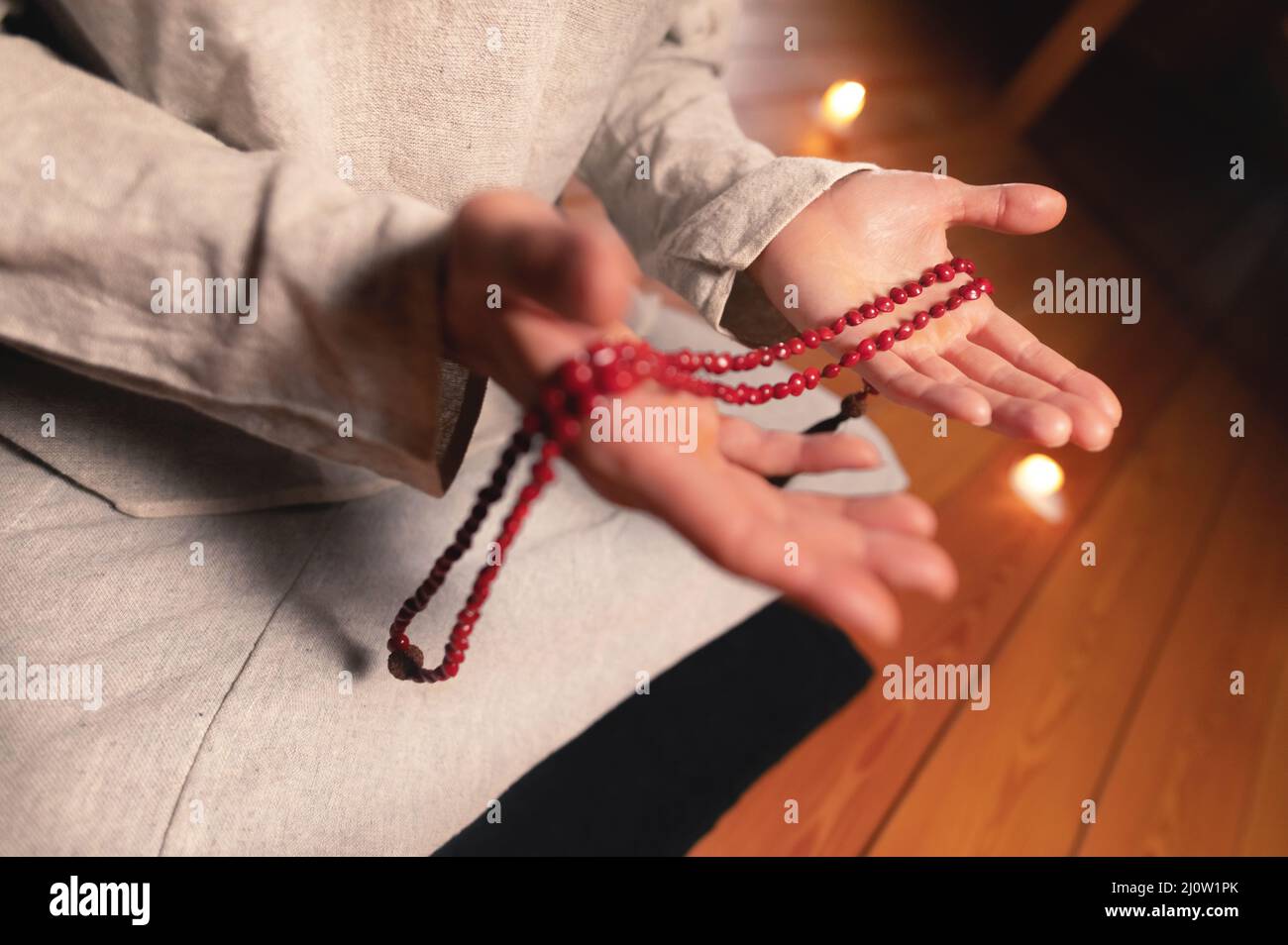 Nahaufnahme Mann in Kleidung für Praxis und Meditation sitzt in einer Lotushaltung und hält roten Rosenkranz, um die Aufmerksamkeit in einem Wald zu konzentrieren Stockfoto