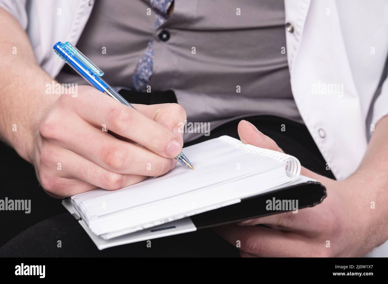 Die Männerhände eines Psychologen in einem weißen Gewand halten ein Notizbuch und einen Kugelschreiber mit einem Notizbuch bereit, um das aufzunehmen Stockfoto