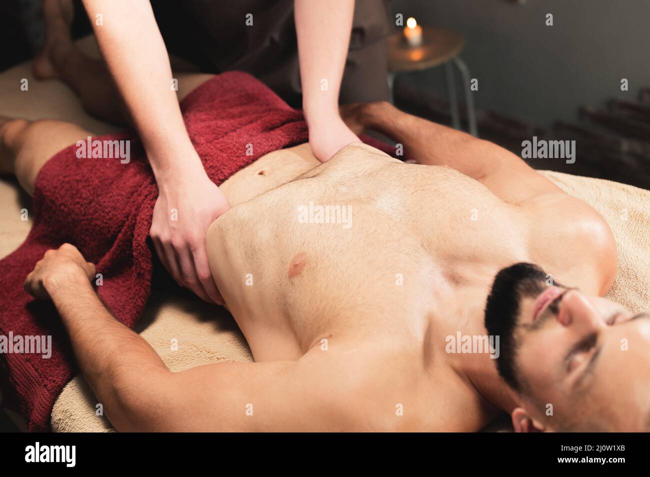 Der männliche Masseur massiert das Thoraxdiaphragma eines muskulösen männlichen Athleten in einem Massageraum mit dunkler Beleuchtung Stockfoto