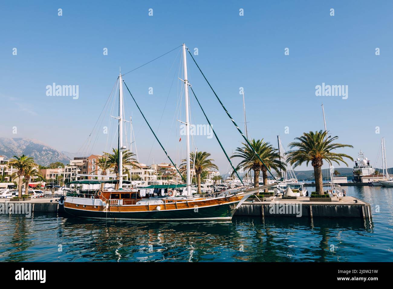 Segelyacht steht am Pier, gesäumt von Palmen im Ferienort Porto. Montenegro Stockfoto