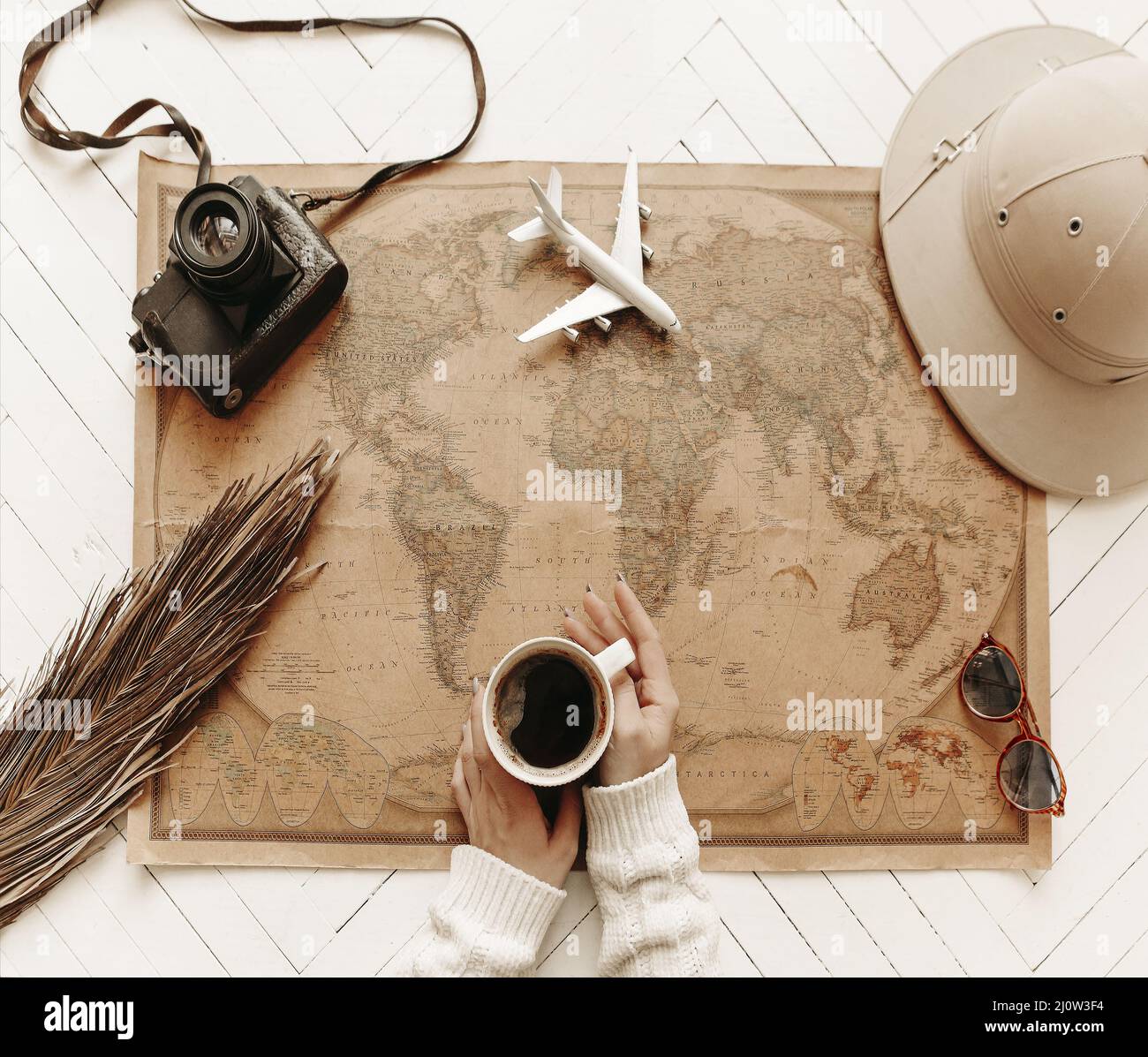Draufsicht auf weibliche Hände Halten Sie eine Tasse schwarzen Kaffee über der Vintage-Weltkarte mit Reisezubehör Stockfoto
