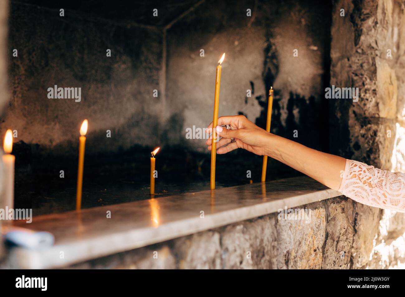 Frau Hand legt eine Wachskerze in eine Nische in einem Tempel Stockfoto