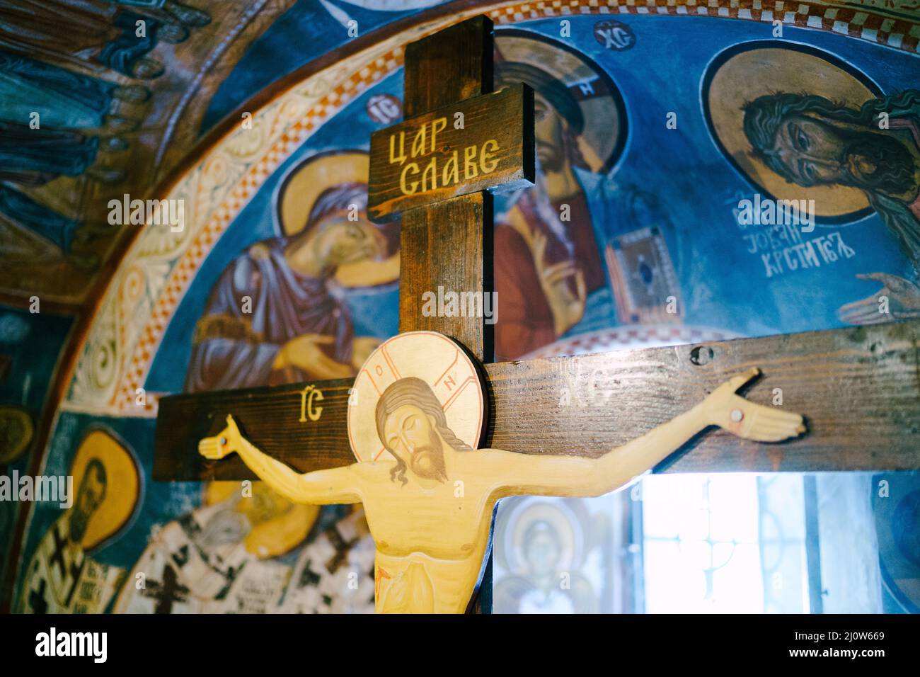 Hölzernes Kruzifix in einer orthodoxen Kirche in der Nähe einer gewölbten Fensteröffnung Stockfoto