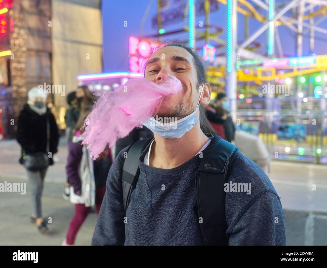 Junger latein, der auf einem Nachtmarkt eine Zuckerwatte isst Stockfoto