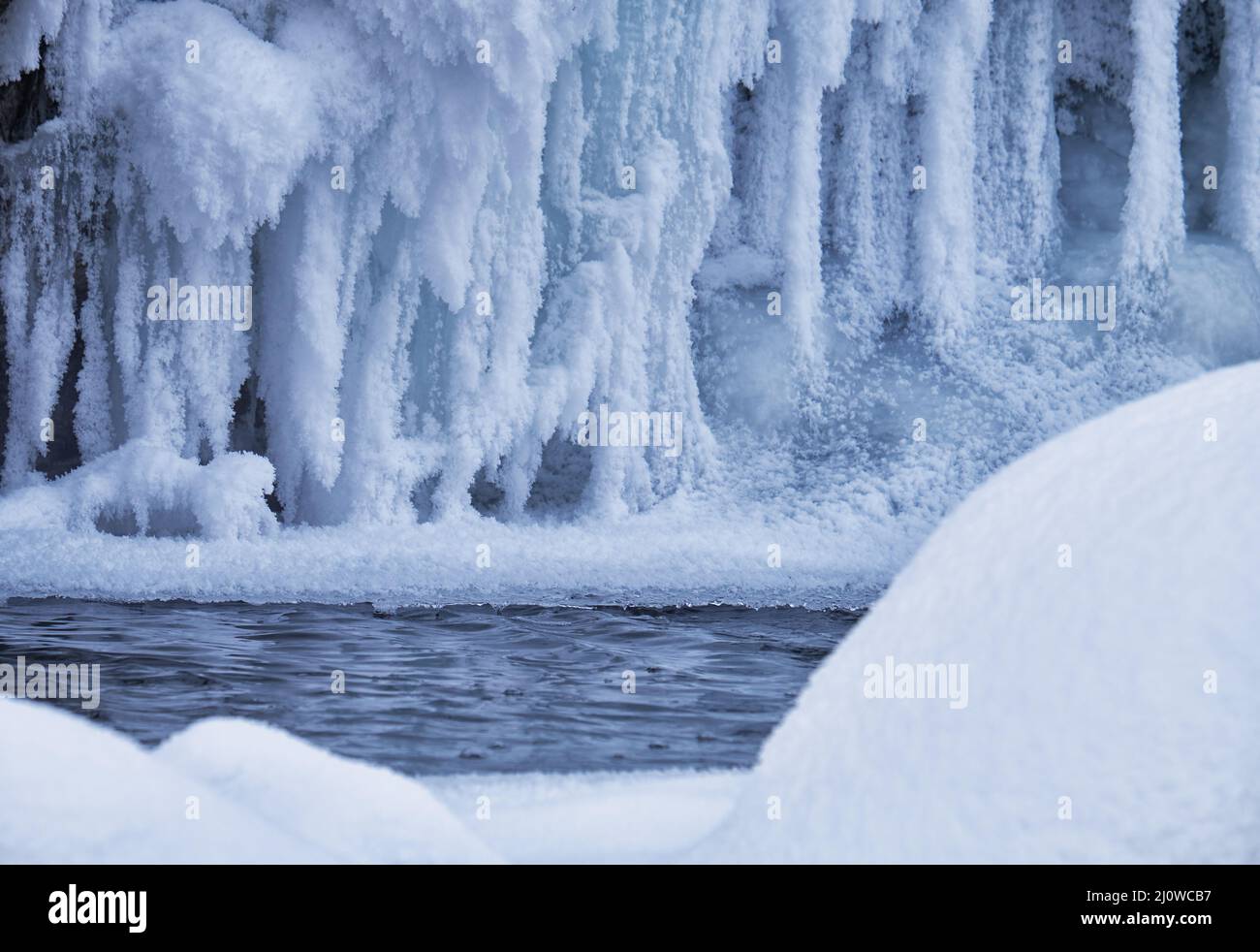 Steine mit Schneekappen und Eis im Wasser des gefrorenen Flusses im Winter. Stockfoto