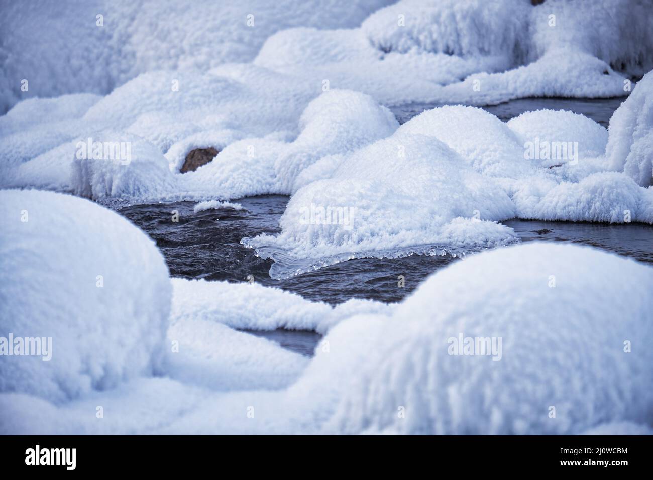 Steine mit Schneekappen und Eis im Wasser des gefrorenen Flusses im Winter. Stockfoto