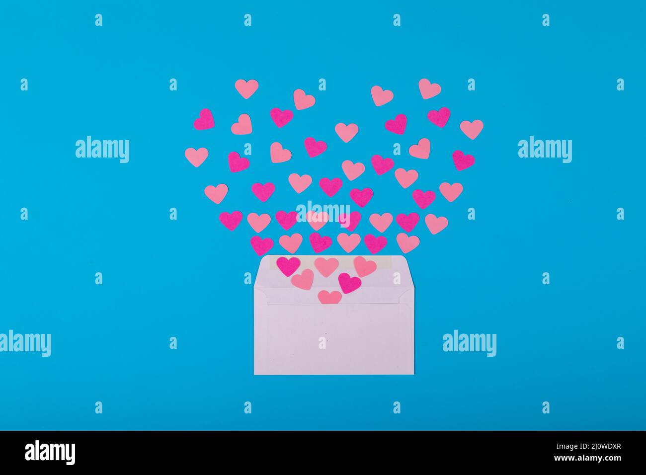 Offener weißer Umschlag mit rosa und pfirsichfarbenen Herzformen auf blauem Hintergrund Stockfoto