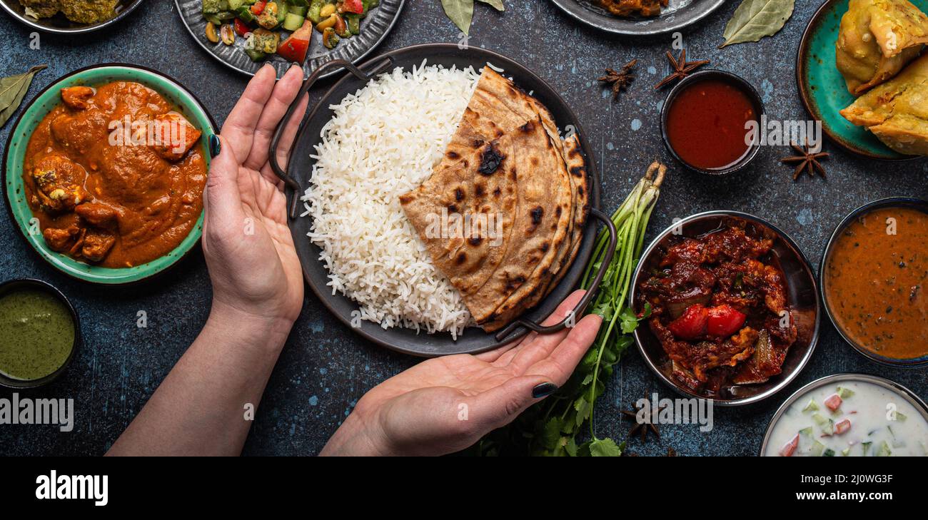 Weibliche Hände servieren ein indisches, ethnisches Buffet auf einem rustikalen Betontisch Stockfoto