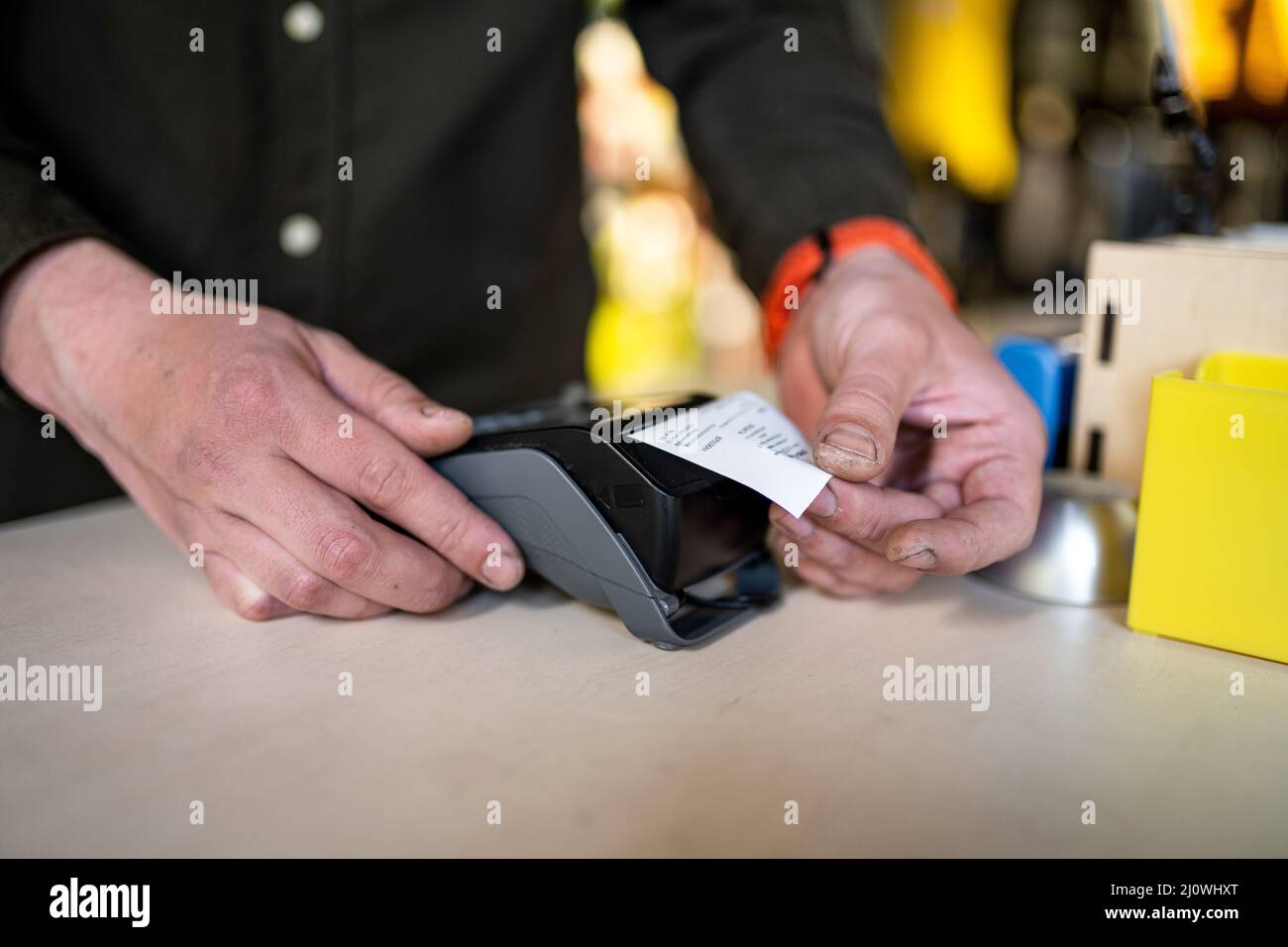 Der Verkäufer hält das Zahlungsterminal, während er den Beleg für den Abschluss des Kaufs hält. Nahaufnahme der Hände. Konzept von NFC, Business und Bank Stockfoto