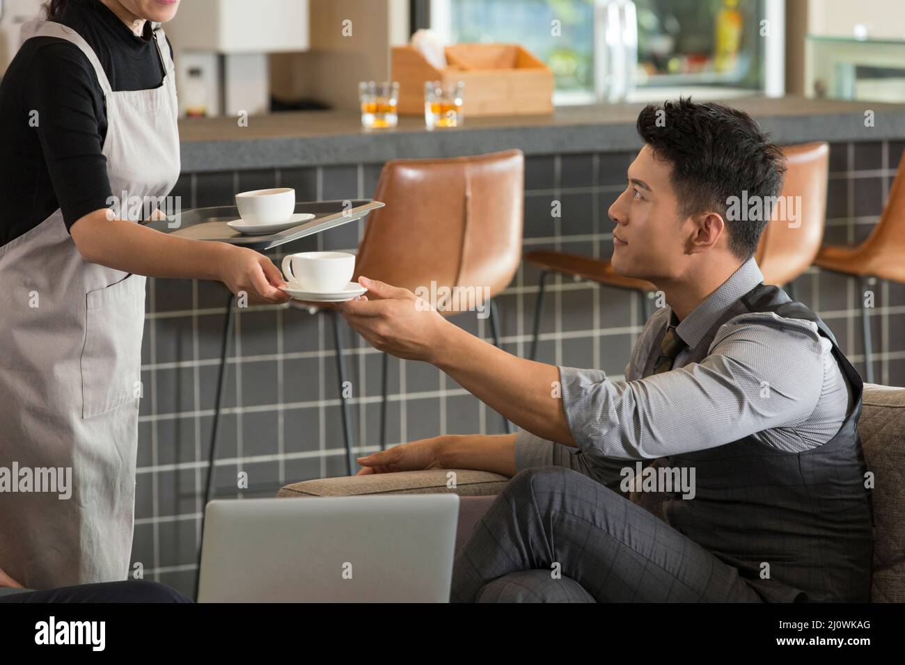 Die junge Kellnerin bietet dem Geschäftsmann eine Tasse Kaffee an Stockfoto