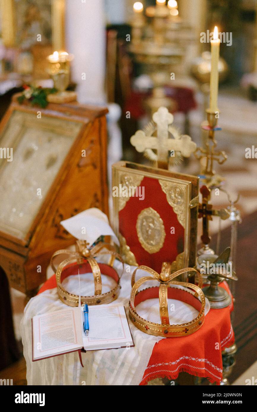 Kreuz, goldene Kronen, Bibel und Kerzenständer stehen auf dem Tisch in der Kirche Stockfoto