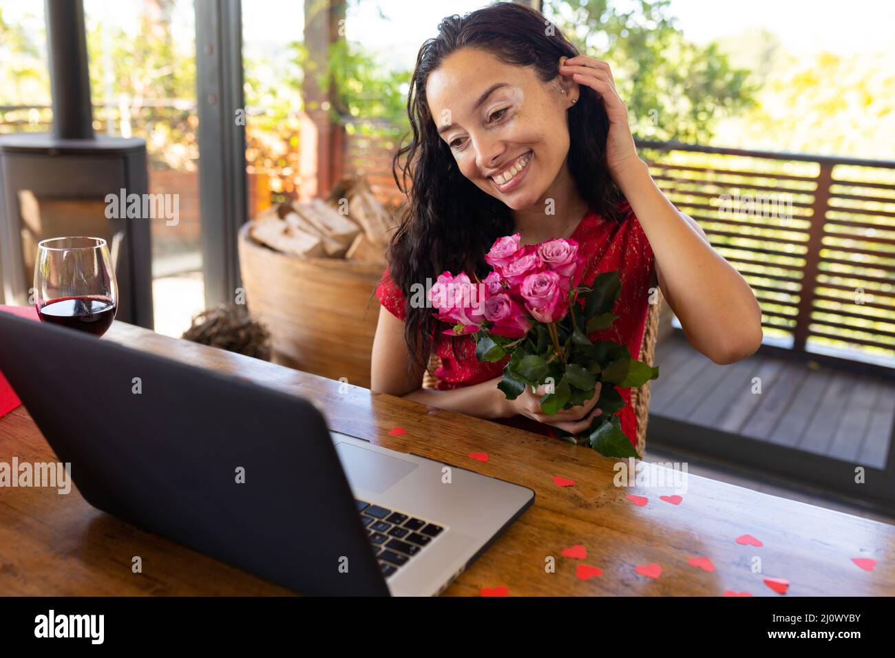 Lächelnde junge Birazialfrau mit Blumenstrauß-Videoanrufen durch Laptop im Restaurant Stockfoto