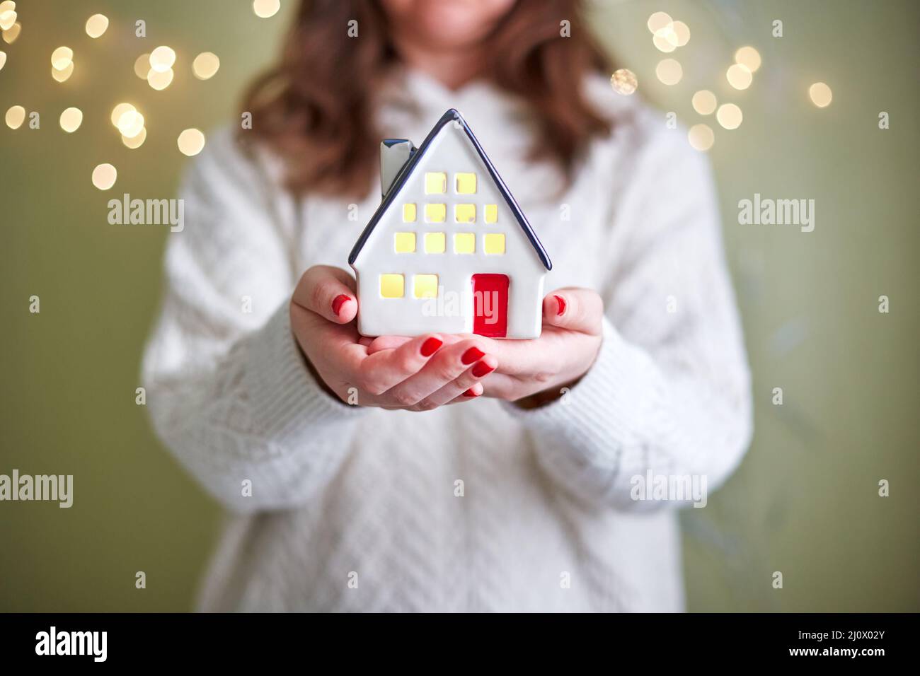 Frau hält in ihren Händen Keramikhaus mit Licht im Inneren. Das Konzept von Urlaub, weihnachten und Gemütlichkeit Stockfoto