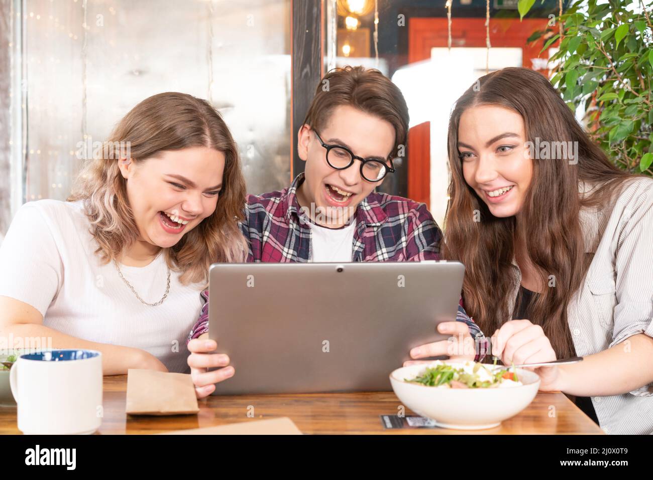 Freunde, die Spaß im Café haben, sehen sich einen Tablet-pc an, sehen sich lustige Videos an oder führen Videoanruf oder soziale Medien. Drei Freunde im Café Stockfoto