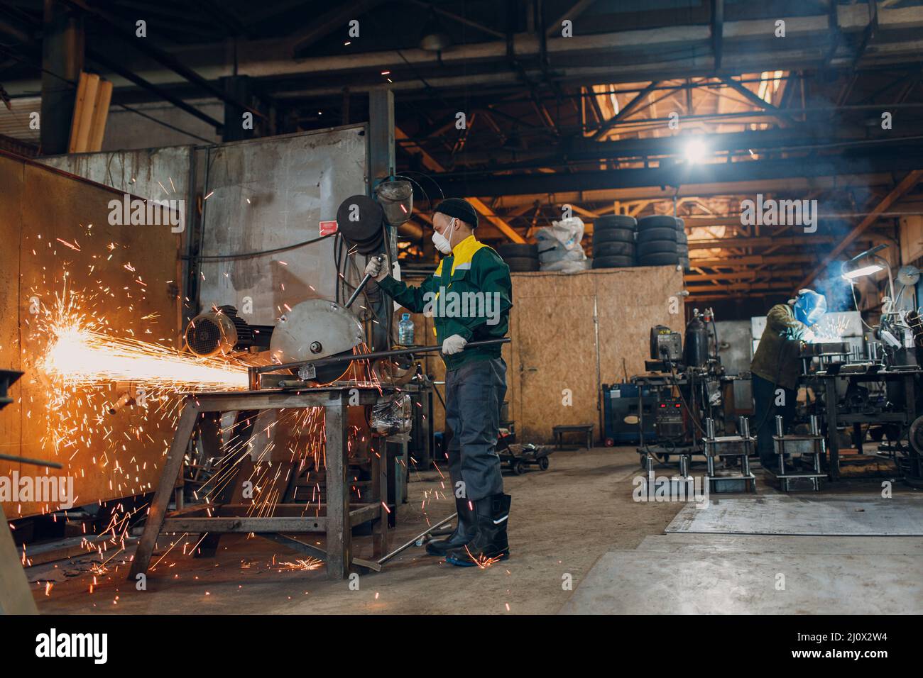 Arbeiter, die im Werk mit Metallkonstruktionen arbeiten. Metallbearbeitung mit großem Winkelschleifer, Scheibensäge und Schweißerschweißen. Funken in Stockfoto