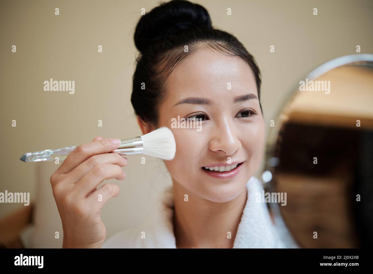 Lächelnde junge Frau, die flüssige Foundation mit synthetischem Make-up Pinsel aufführt Stockfoto