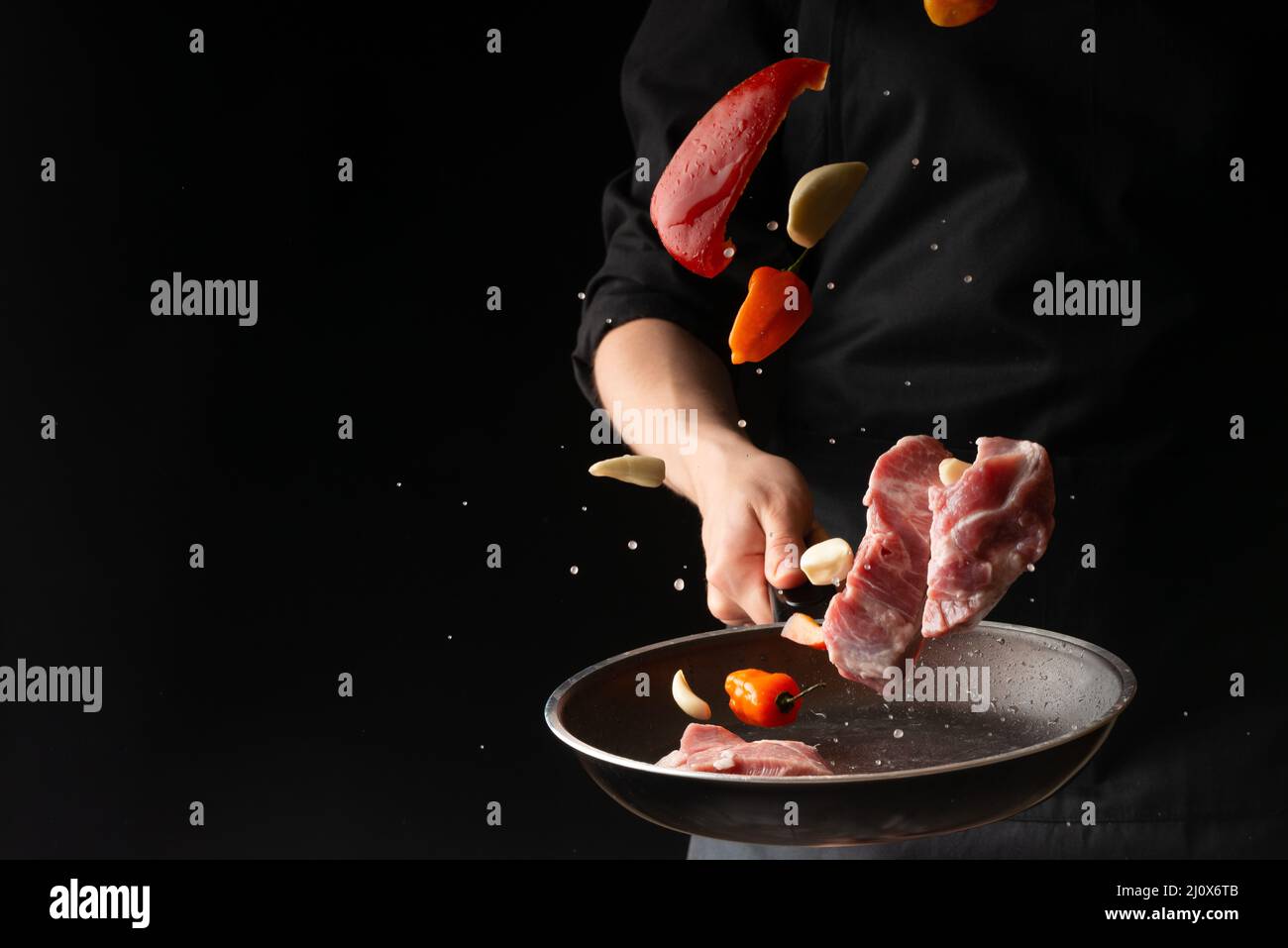 Der Küchenchef bereitet Steaks aus Fleisch, Schwein oder Rind zu und wirft frisches Fleisch mit Paprika und Knoblauch auf schwarzem Hintergrund in einer Pfanne, horizontal Pho Stockfoto