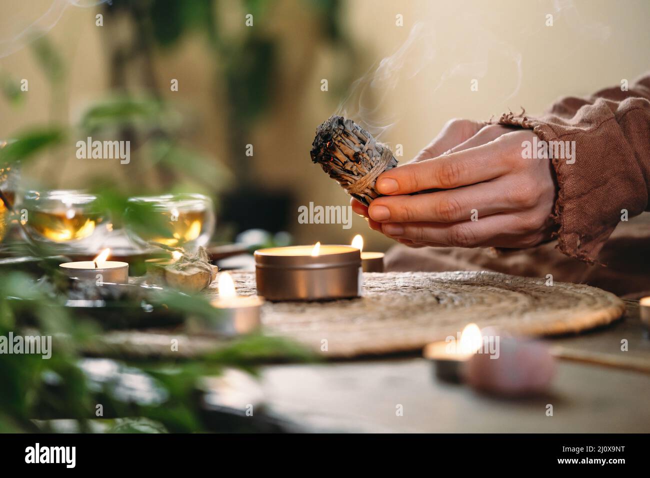 Frau Hände brennen weißen Salbei, vor dem Ritual auf dem Tisch mit Kerzen und grünen Pflanzen. Smoke of smudging behandelt Schmerzen und Stress, klar negativ Stockfoto