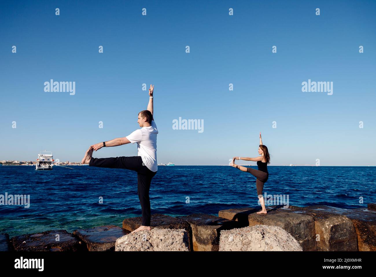 Mann und Frau machen Yoga vor dem Hintergrund des Meeres und des blauen Himmels. Konzept Einsamkeit mit der Natur, Selbstakzeptanz, Liebe und Unterstützung. Stockfoto