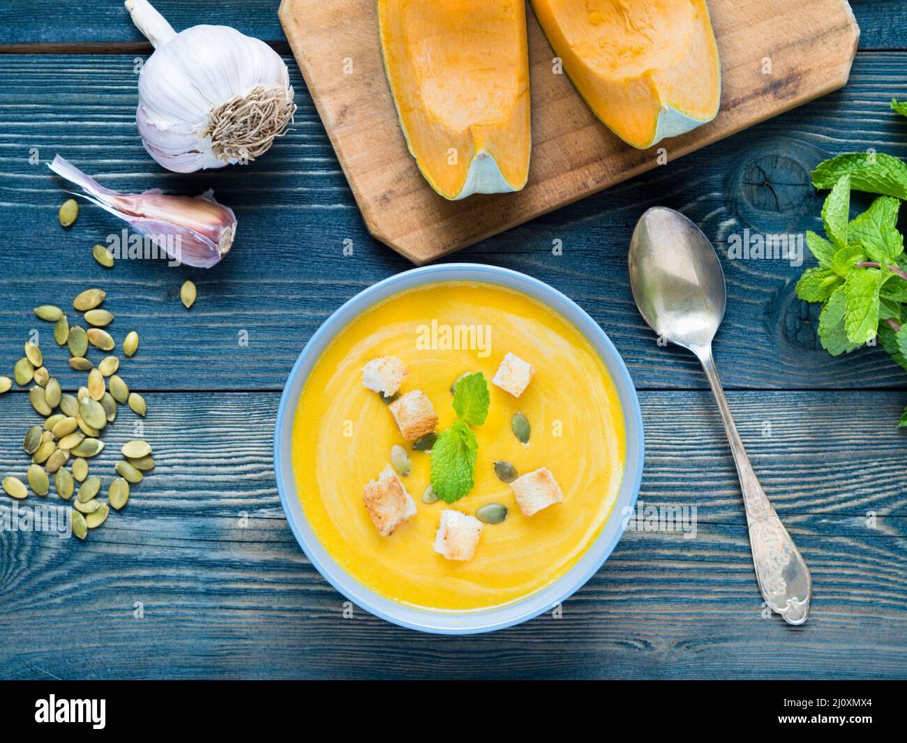 Von Kürbis cremige Suppe mit Croutons und Samen auf dunkelblauem Hintergrund Holz, Knoblauch, Minze, kürbisscheiben. Ansicht von oben. Stockfoto
