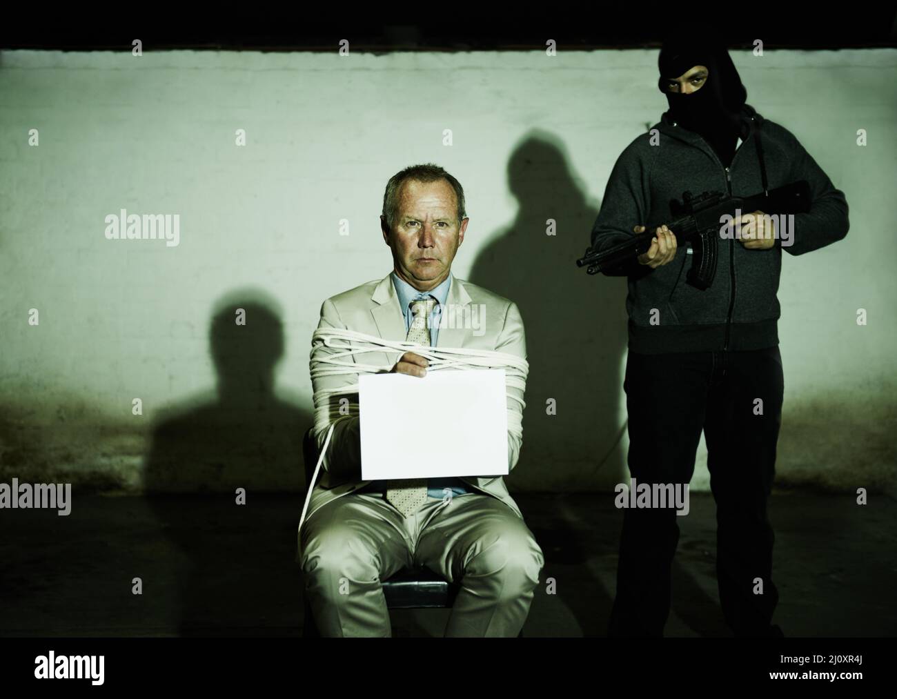 Ihre Forderungen offenlegen. Ein entführter Geschäftsmann, der ein Plakat mit den Forderungen seiner Angreifer hält. Stockfoto