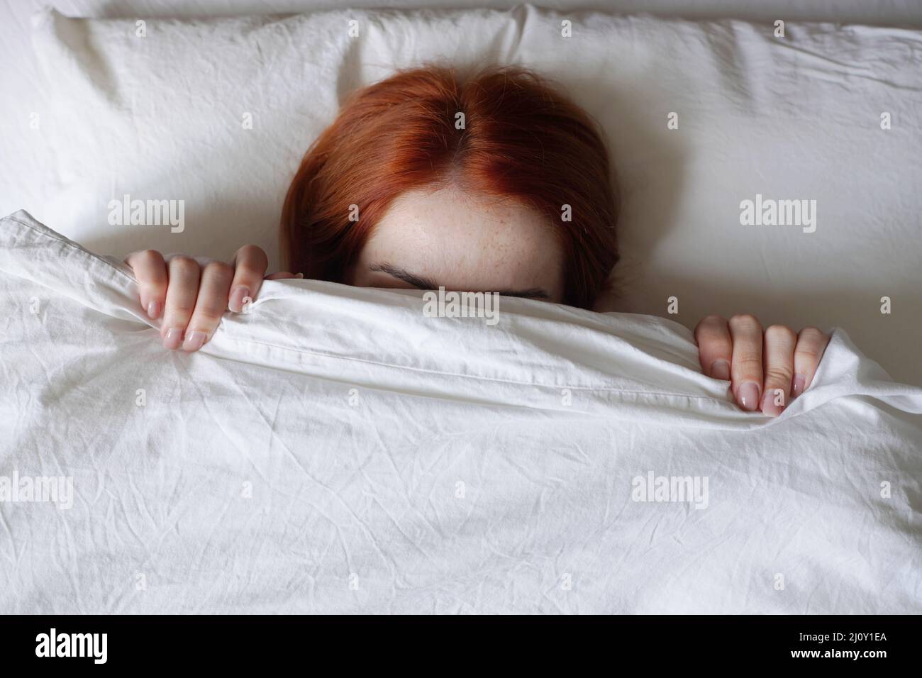 Frau, die das Gesicht vor Sonnenlicht unter der Bettdecke versteckt Stockfoto