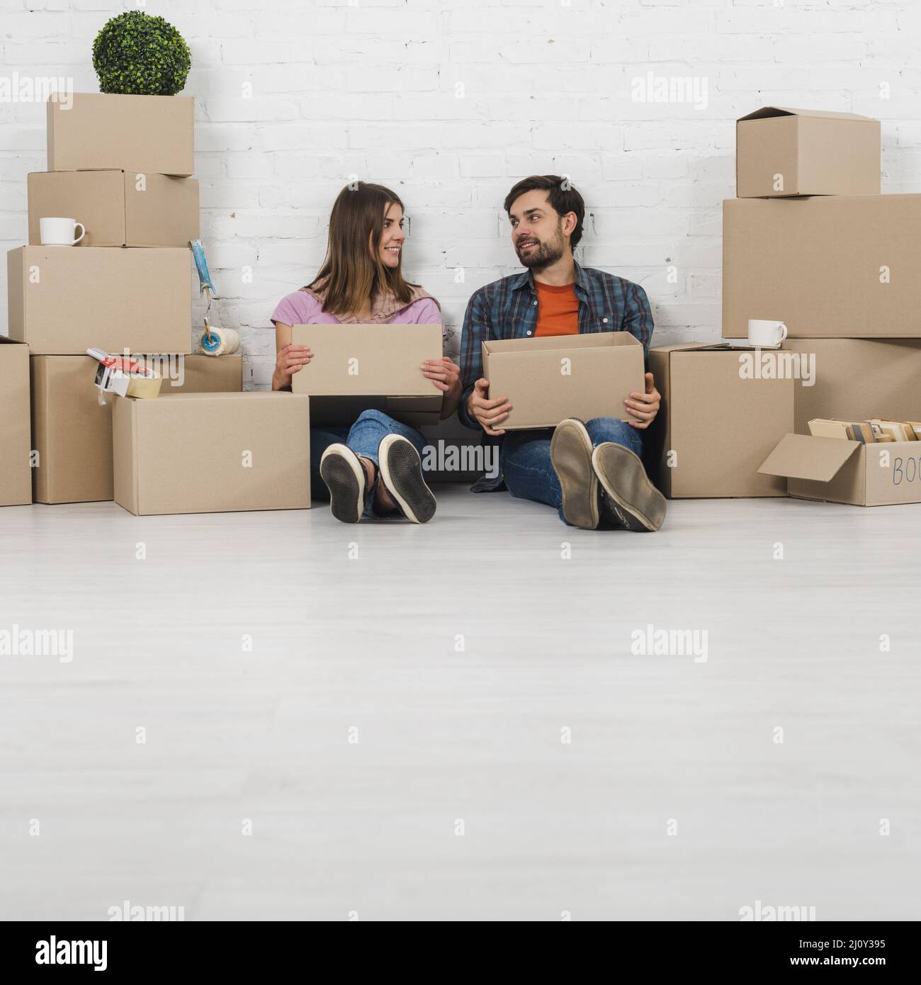 Junges Paar sitzend Boden hält Pappkartons Hand suchen einander. Hochwertige Fotos Stockfoto