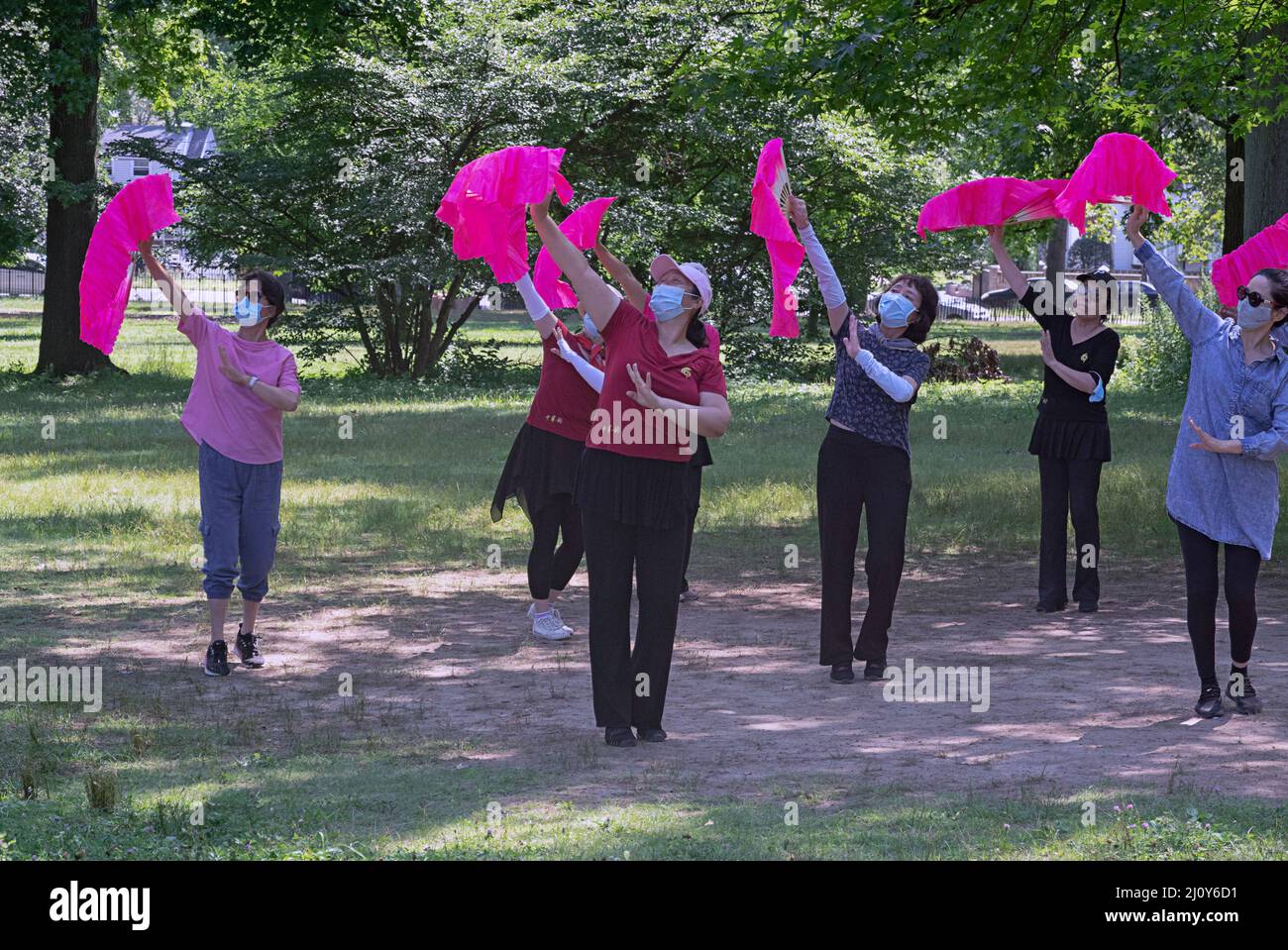 Chinesische amerikanische Frauen mittleren Alters nehmen an einem Tai-Chi-Kurs in einem Park Teil, während sie Masken tragen. An einem warmen Sommertag im Jahr 2021. Stockfoto