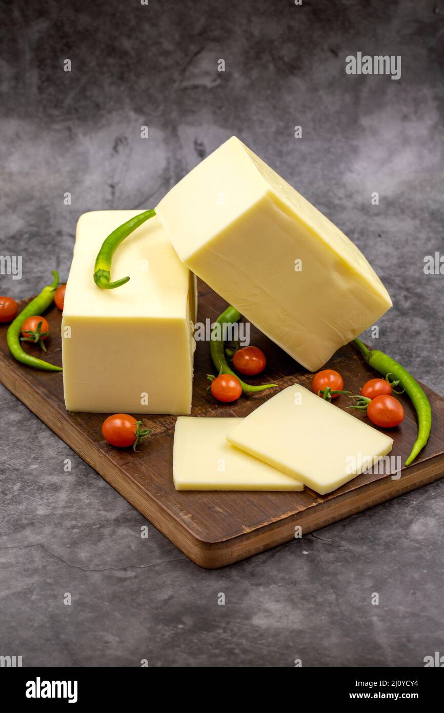 Cheddar-Käse oder Kashkaval-Käse auf dunklem Hintergrund. Käsescheiben auf dem Servierbrett Stockfoto