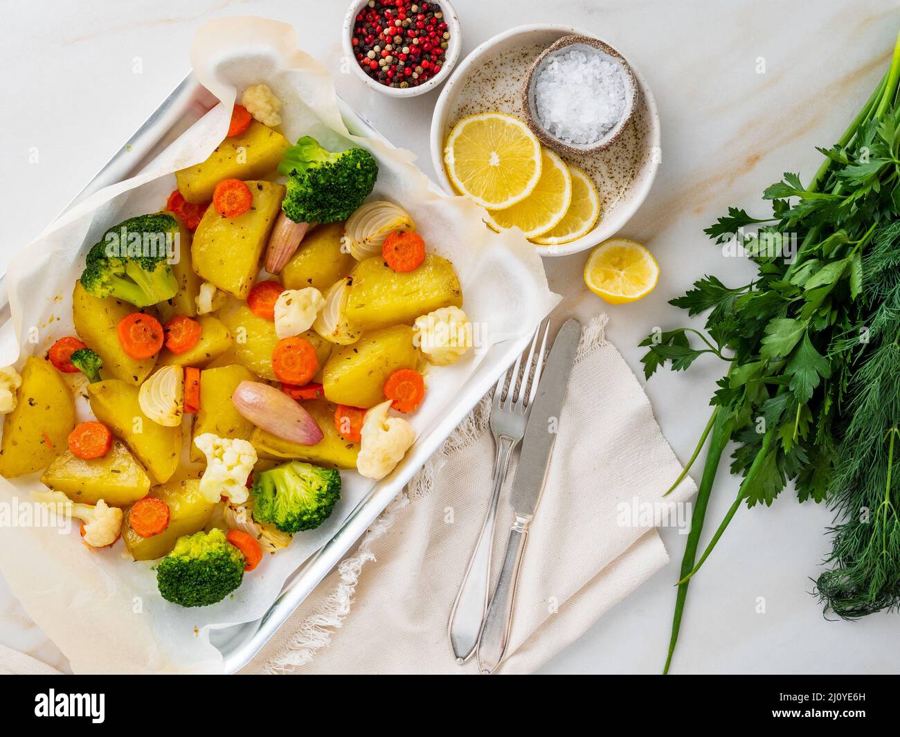 Gebratenes Gemüse auf Tablett mit Pergament auf Marmortisch. Kartoffeln, Karotten, Stockfoto