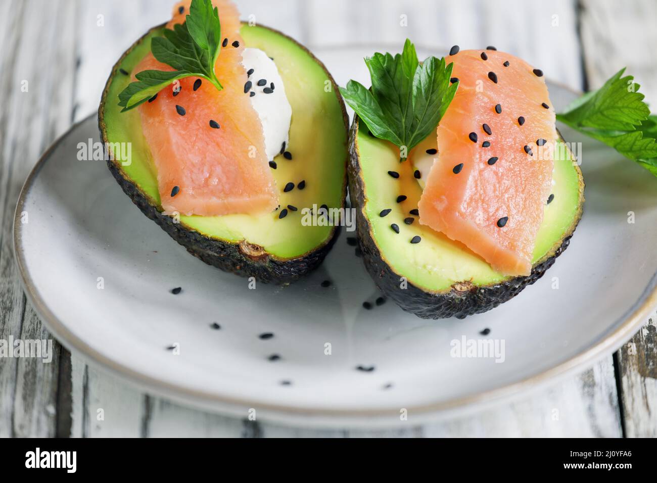 Beliebte Keto-Diät-Mahlzeit aus geräuchertem Lachs, frischen Avocado- und Frischkäsebooten, garniert mit schwarzen Sesamsamen und Petersilie. Ein gesundes Mittagessen oder Stockfoto
