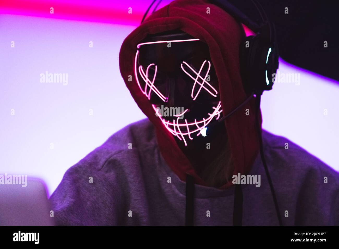 Cyber-Sicherheitskonzept. Anonymer Hacker in einer beängstigenden Maske mit Kopfhörern und Laptop. Hochwertige Fotos Stockfoto