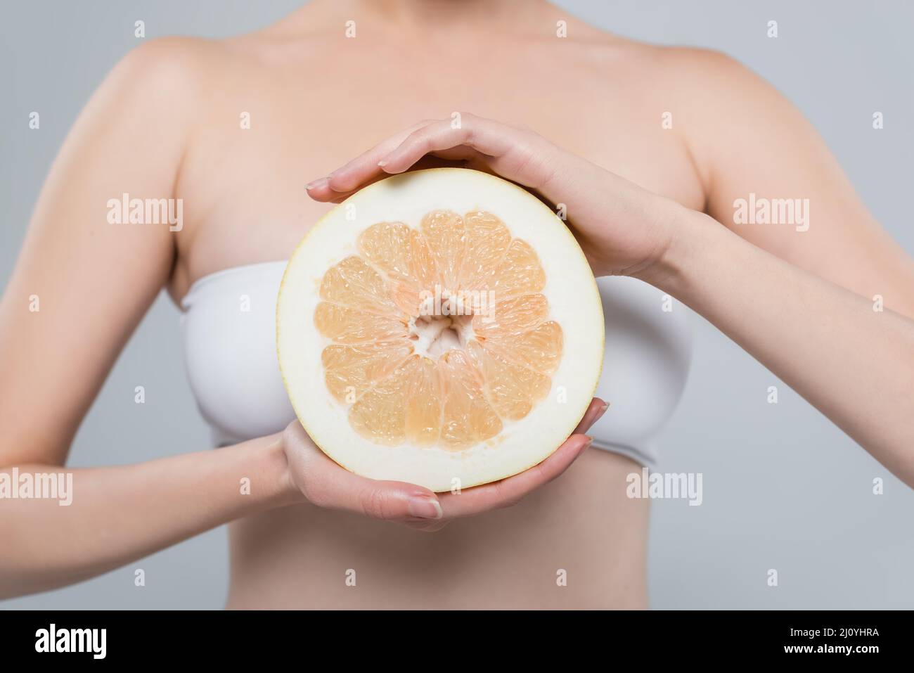 Beschnittene Ansicht einer Frau mit einer Hälfte reifer Grapefruit, isoliert auf Grau Stockfoto