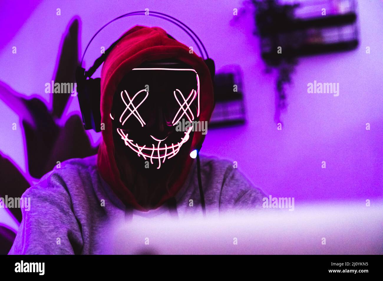 Cyberspace-Schutzkonzept. Hacker tragen eine unheimliche Maske, Kopfhörer und einen Hoodie. Magentafarbener Hintergrund. Hochwertige Fotos Stockfoto