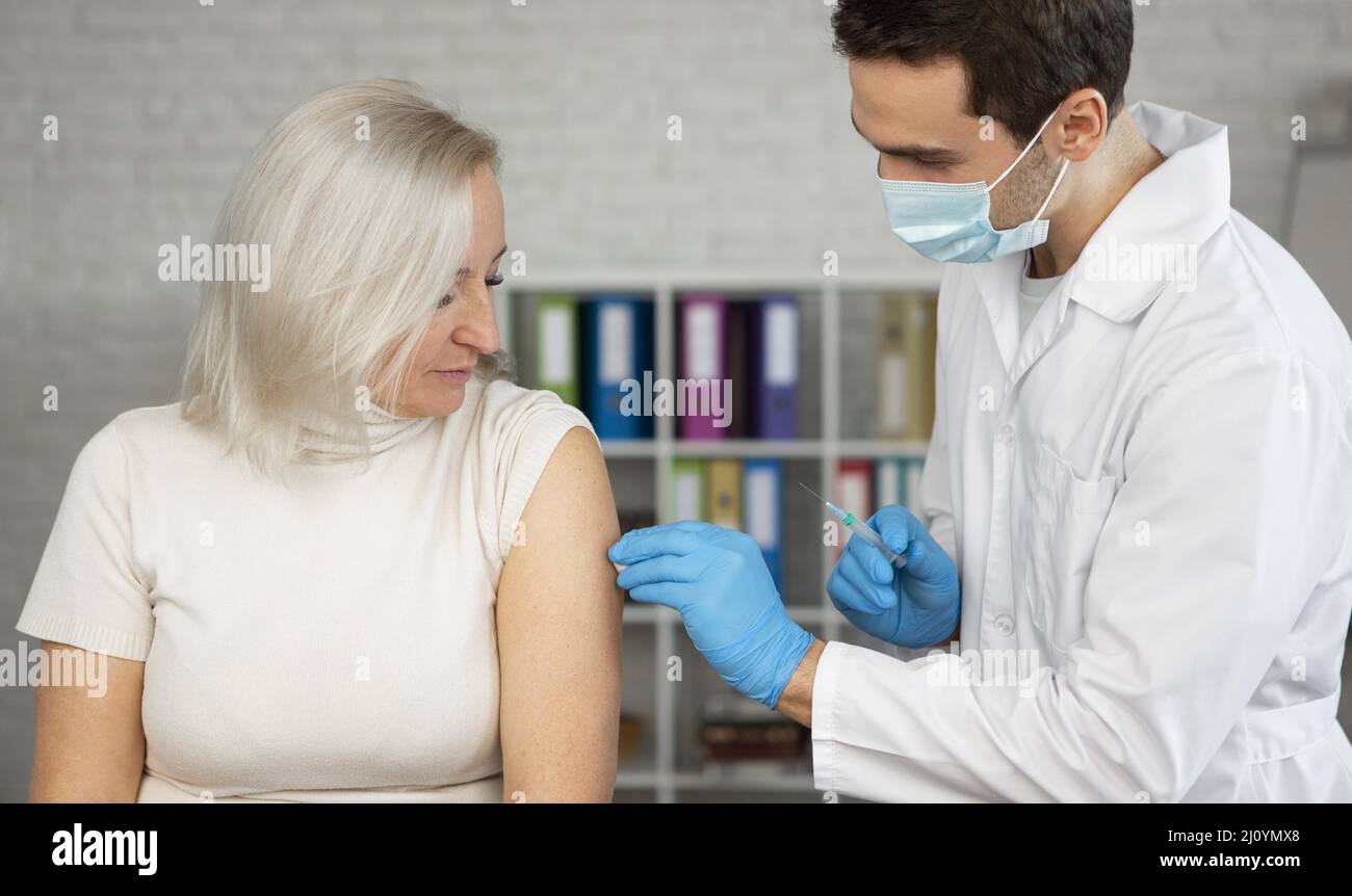 Arzt mit mittlerer Schussaufnahme, der den Impfstoff verabreicht. Hochwertige Fotos Stockfoto