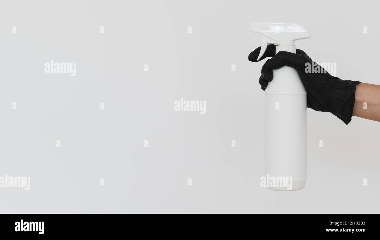 Hand mit Handschuh, der die Desinfektionsflasche mit Kopierraum hält Stockfoto