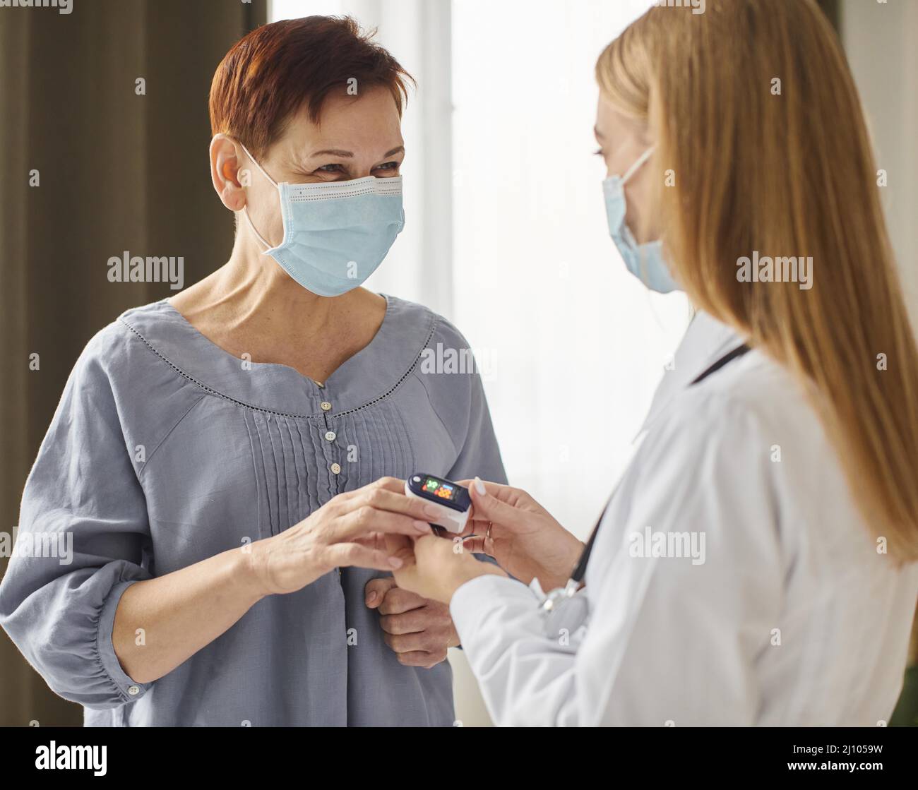 Covid-Genesungszentrum Ärztin mit medizinischer Maske zur Überprüfung des Sauerstoffgehalts des älteren Patienten Stockfoto