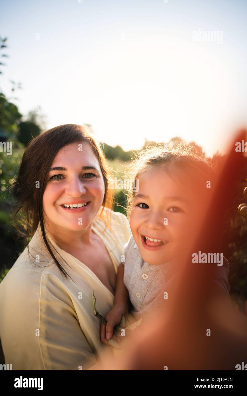 Die europäische Mutter und ihre asiatische Tochter im Sommer im Apfelgarten Stockfoto