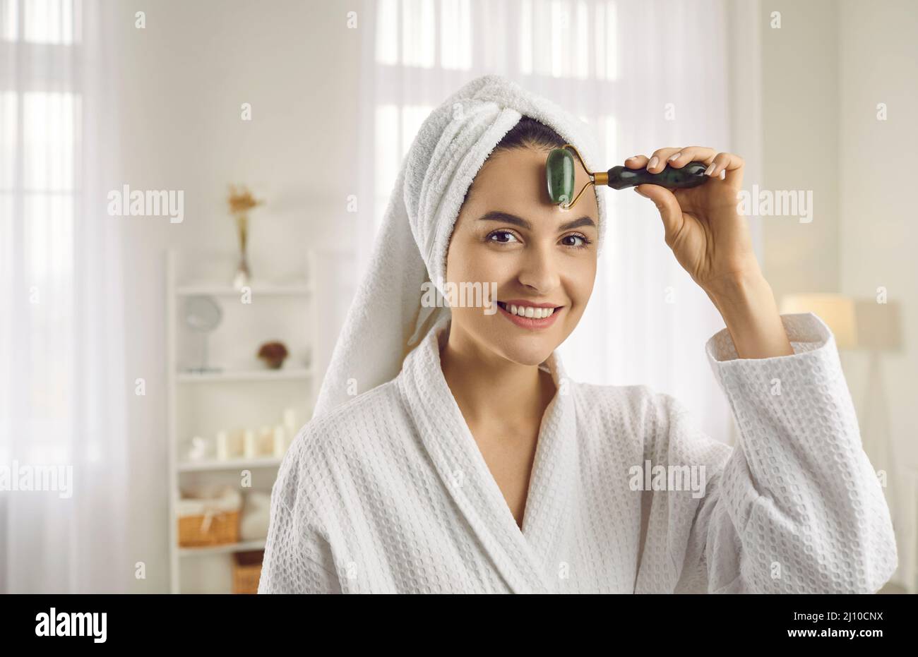 Junge Frau massiert Gesicht mit Jaderolle, um die Lymphe zu entleeren und die Blutzirkulation zu erhöhen Stockfoto