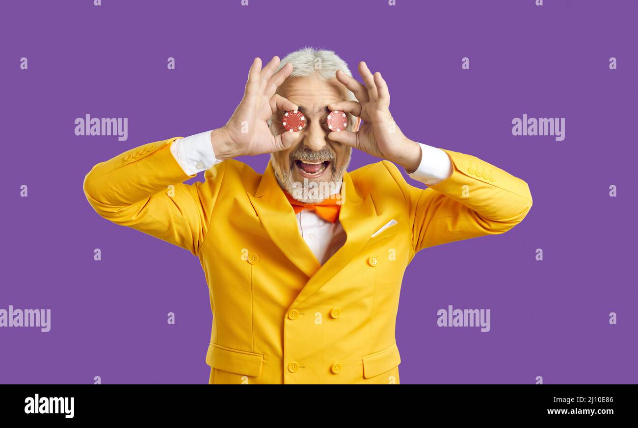 Porträt eines lustigen glücklichen älteren Mannes in gelbem Anzug, der seine Augen mit zwei Pokerchips bedeckt Stockfoto