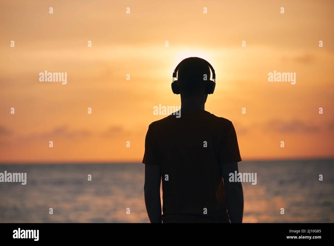 Silhouette eines Mannes mit Kopfhörern gegen den Ozean. Gelassenheit, Kontemplation und Musik beim goldenen Sonnenuntergang. Stockfoto
