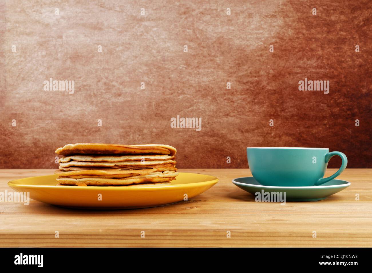 Stapel von hausgemachten Pfannkuchen auf einem gelben Teller und eine Tasse Kaffee oder Tee auf einem Holztisch. Copyspace. Stockfoto