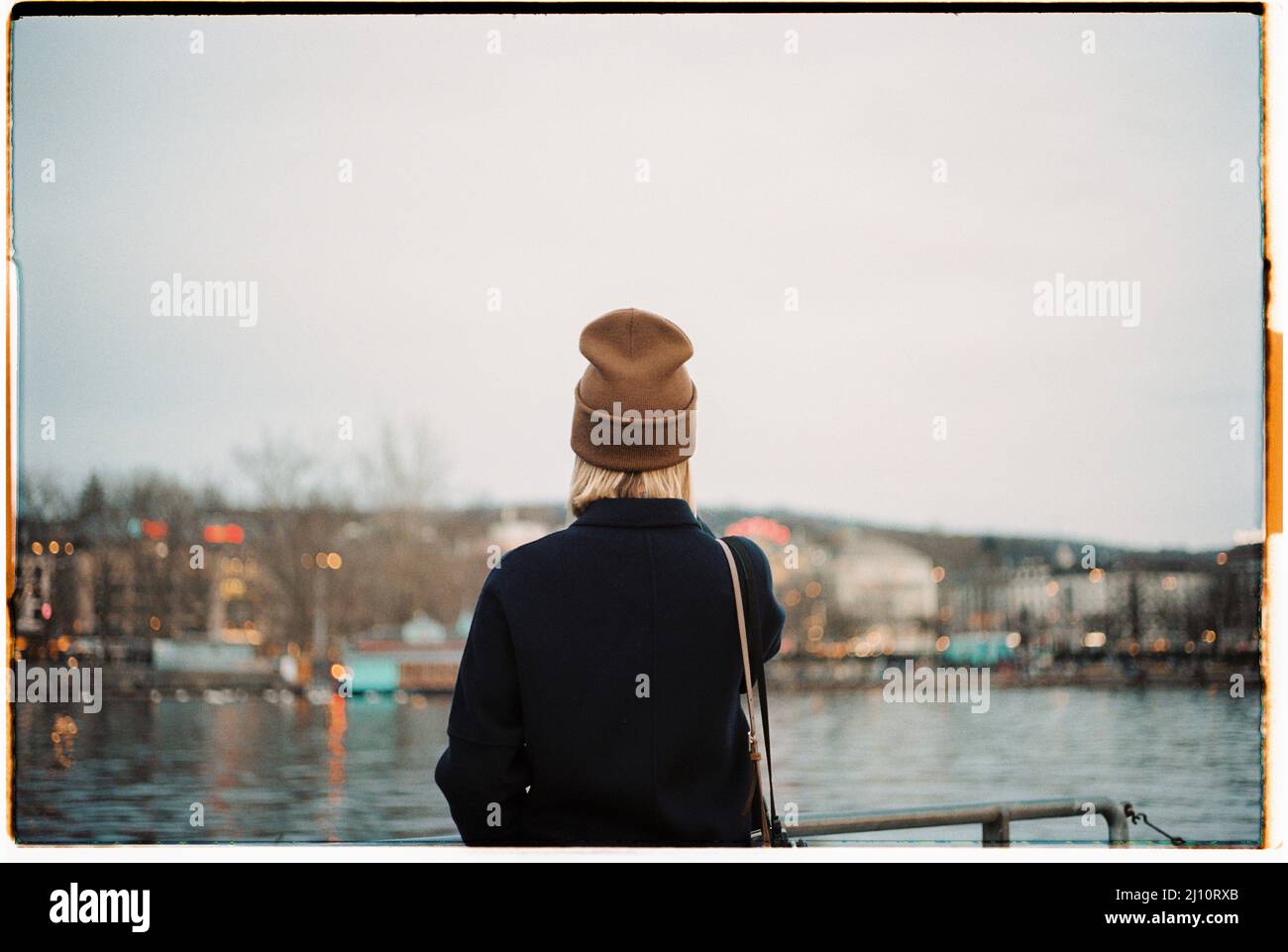 Frau in winterlicher dunkler Kleidung mit Blick nach hinten auf den Genfer See Stockfoto